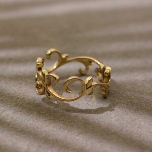 May include: A gold ring with an intricate filigree design. The ring showcases delicate floral and scrollwork patterns, giving it a vintage look. The ring is displayed on a neutral background.