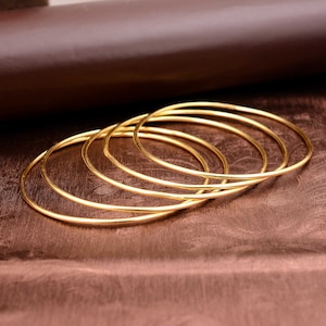May include: A set of five gold-toned bangle bracelets stacked on top of each other. The bracelets are smooth and shiny.