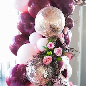 May include: A balloon arch made of pink and burgundy balloons with gold glitter balloons and pink flowers.