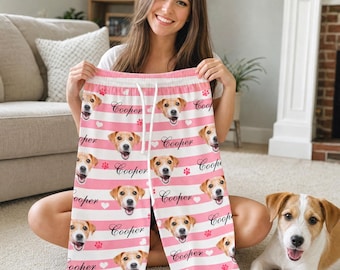 Pode incluir: Calças de pijama às riscas brancas e cor-de-rosa com um padrão repetitivo da cara de um cão, o nome Cooper em letra cursiva preta, pequenos corações brancos e pegadas de patas cor-de-rosa. Cintura com cordão ajustável branco.