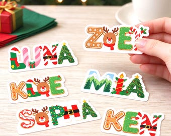 Pode incluir: Uma coleção de adesivos de vinil cortados com nomes formados por letras com temas festivos de Natal. Os designs incluem pão de mel, renas, bengalas doces, árvores de Natal e cintos de Papai Noel em vermelho, verde e branco.