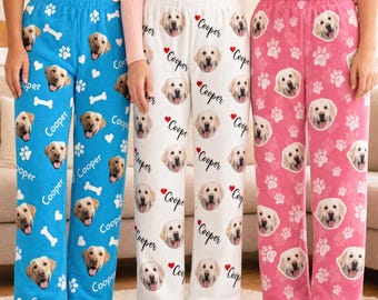 Pode incluir: Três calças de pijama em azul, branco e rosa, cada uma com um padrão repetitivo de rostos de golden retriever, pegadas e ossos. As calças brancas também incluem o nome Cooper impresso em preto ao lado de um coração vermelho.