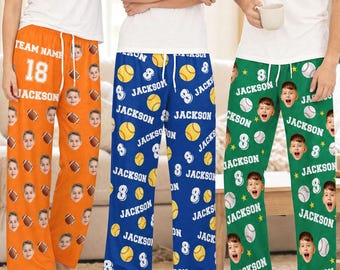 Pode incluir: Três calças de descanso em laranja, azul e verde, cada uma com um padrão repetitivo de um rosto, o nome Jackson, o número 8 e bolas de basebol. O par laranja também exibe o texto Team Name 18 Jackson.