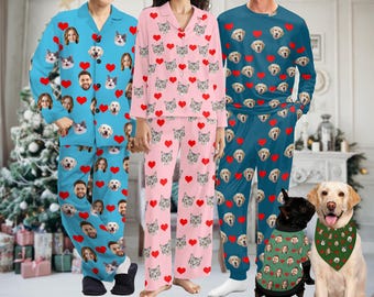 May include: Three pairs of pajamas with a heart pattern featuring different faces of people and pets. The pajamas are in blue, pink, and teal colors. The pajamas are long-sleeved and have a button-up top. There are two dogs in the image, one wearing a green bandana with a face pattern and the other wearing a green bandana with a face pattern.