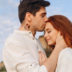 Pu&ograve; includere: Una coppia si abbraccia, l'uomo bacia la fronte della donna. L'uomo ha un tatuaggio sul collo che dice "Finalmente" con un piccolo cuore rosso.