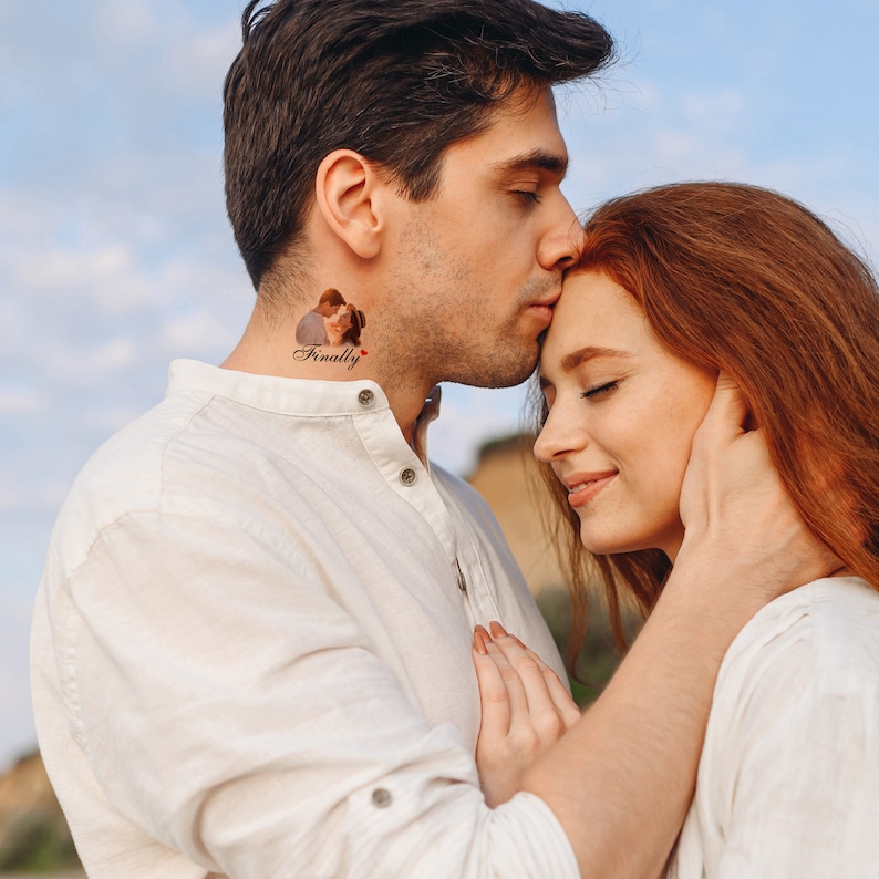 Pu&ograve; includere: Una coppia si abbraccia, l'uomo bacia la fronte della donna. L'uomo ha un tatuaggio sul collo che dice "Finalmente" con un piccolo cuore rosso.