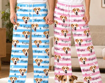 Pode incluir: Dois pares de calças de pijama com um padrão repetitivo do rosto de um cão e o nome Cooper. Um par tem riscas horizontais azuis e brancas com pegadas azuis, enquanto o outro tem riscas cor-de-rosa e brancas com pegadas cor-de-rosa.