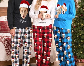 Pode incluir: Três conjuntos de pijama de manga comprida com fotos personalizadas de rostos usando gorros de Pai Natal. A camisola preta mostra a Sophia, a branca o Ronald e a azul o Milo e o Cooper com calças de xadrez a combinar.