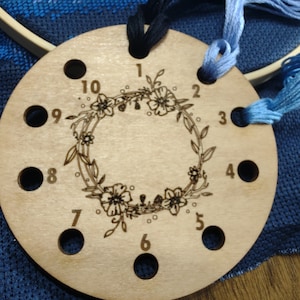 May include: A wooden thread organizer with ten numbered holes and a floral design. The organizer is used for holding embroidery floss.