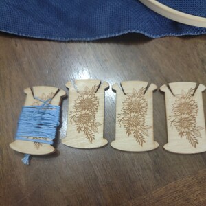 May include: Four wooden thread bobbins with a sunflower design. One bobbin is wound with light blue thread.