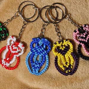 Könnte beinhalten: Fünf bunte Schlüsselanhänger aus geknüpfter Schnur mit silbernen Schlüsselringen. Die Schlüsselanhänger sind in den Farben Grün, Rot, Blau, Gelb und Pink.