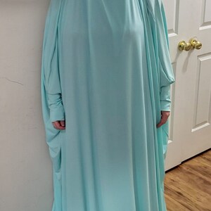 Puede incluir: Una t&uacute;nica de oraci&oacute;n azul claro con mangas largas. La t&uacute;nica est&aacute; hecha de una tela suave y fluida.