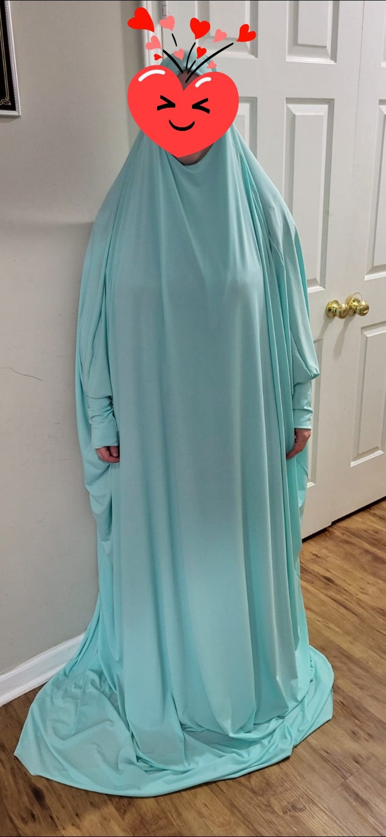 Puede incluir: Una t&uacute;nica de oraci&oacute;n azul claro con mangas largas. La t&uacute;nica est&aacute; hecha de una tela suave y fluida.