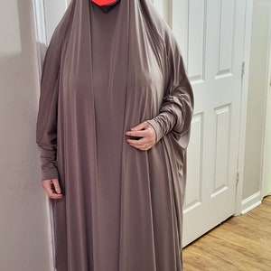 Puede incluir: Una abaya larga, holgada, de color marr&oacute;n, de punto de jersey, con mangas largas y cuello alto.