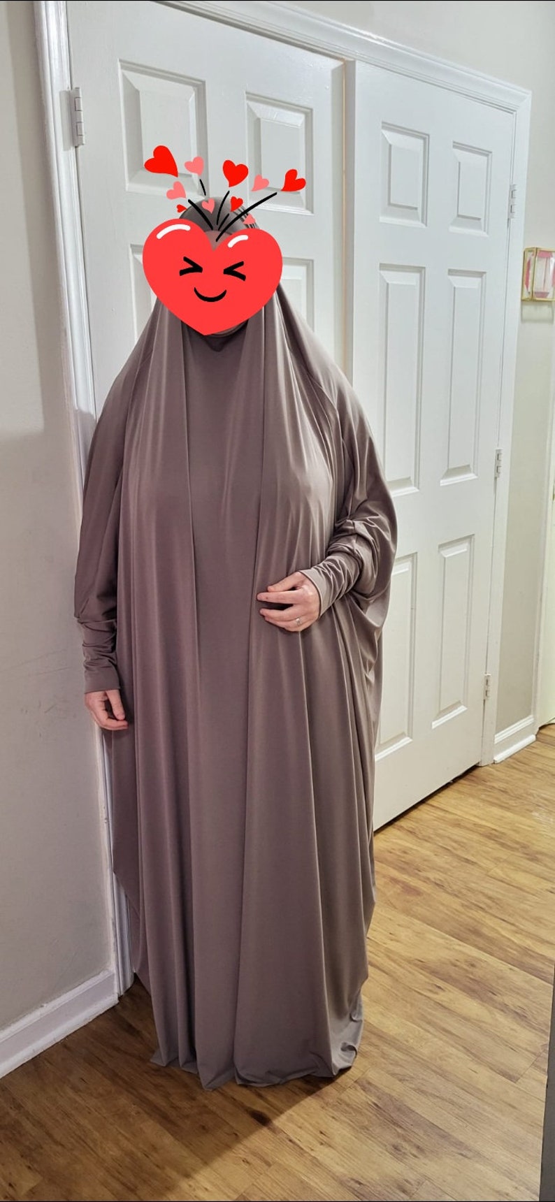 Puede incluir: Una abaya larga, holgada, de color marr&oacute;n, de punto de jersey, con mangas largas y cuello alto.