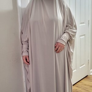 Puede incluir: Una prenda de vestir de color gris claro, de manga larga, holgada y con cuello alto. La prenda est&aacute; hecha de una tela suave y fluida y tiene un ajuste holgado.