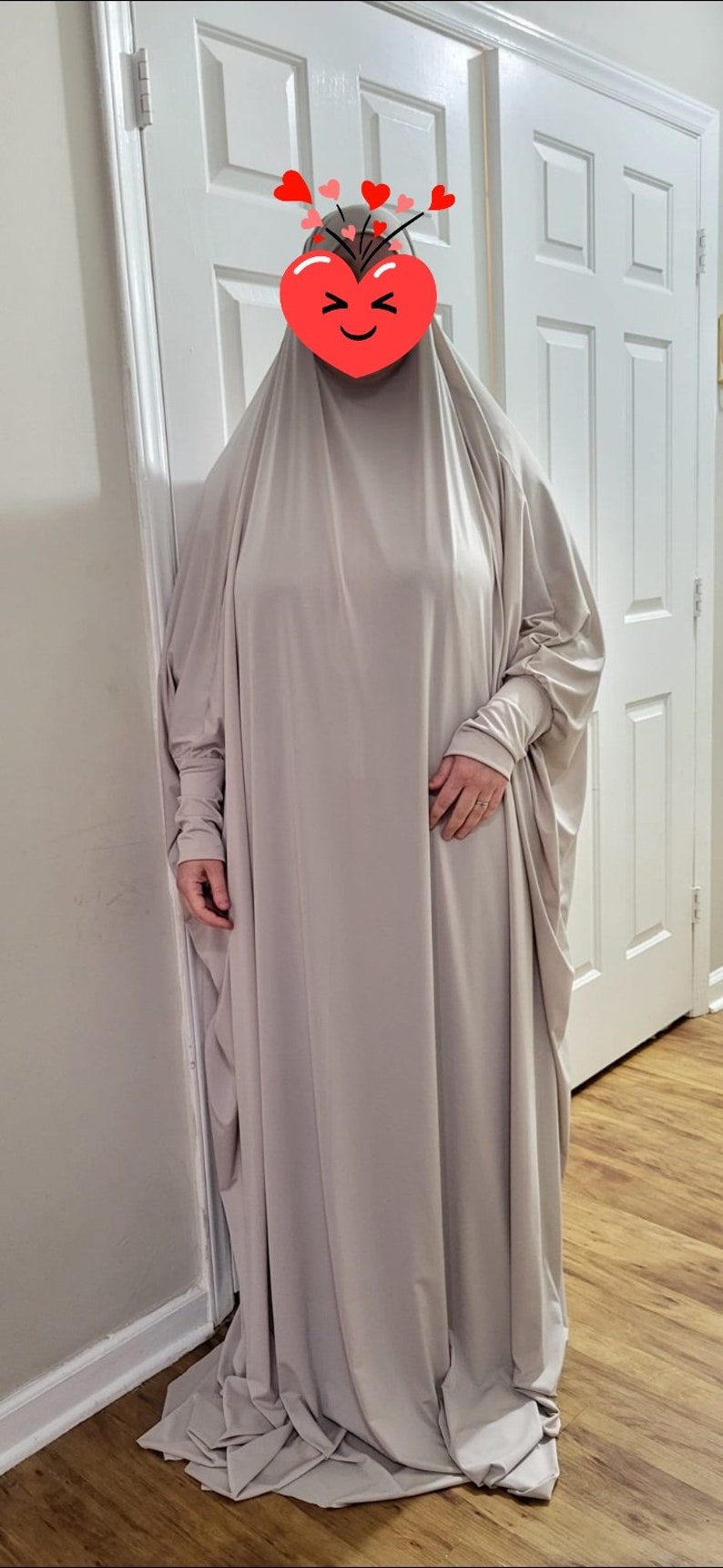 Puede incluir: Una prenda de vestir de color gris claro, de manga larga, holgada y con cuello alto. La prenda est&aacute; hecha de una tela suave y fluida y tiene un ajuste holgado.