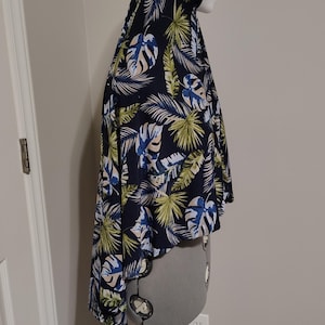 May include: A dark blue head covering with a tropical leaf pattern in shades of green, blue, and cream. The fabric is draped over a mannequin head and shoulders. The garment has a hood and a flowing, cape-like design.