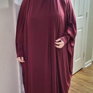 Puede incluir: Una prenda de vestir de color burdeos, de manga larga, holgada y con cuello alto. La prenda est&aacute; hecha de una tela suave y fluida.