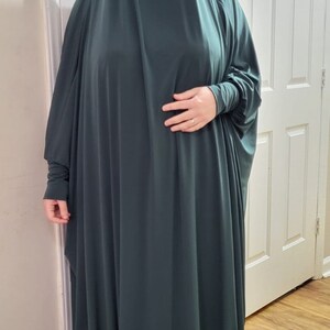 Puede incluir: Una prenda de vestir de color verde oscuro, de manga larga y holgada, con cuello alto. La prenda est&aacute; hecha de un tejido suave y el&aacute;stico y tiene un dise&ntilde;o fluido y drapeado.