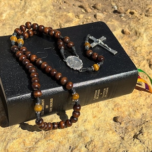 May include: A brown wooden rosary with tiger's eye beads and a silver crucifix resting on a black leather-bound book titled "The Liturgy of the Hours: Lenten & Easter Season".
