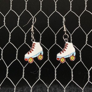 May include: A pair of silver roller skate earrings with white and blue skates and yellow wheels. The earrings are hanging from a wire mesh background.