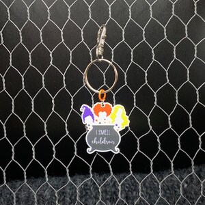 May include: A black cauldron keychain with three witches and the text "I smell children". The keychain is attached to a silver key ring.