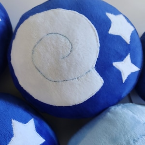 Op de afbeelding: Vijf blauwe en witte pluche ballen met verschillende ontwerpen. De ballen hebben witte sterren en een wit schelpontwerp.