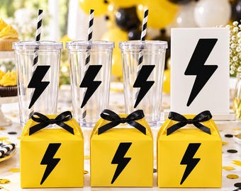 May include: Three clear plastic tumblers with black and white striped straws, each featuring a black lightning bolt decal. Three yellow gift boxes with black ribbon bows and black lightning bolt icons, plus a white sign with a black bolt.