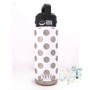 May include: A white Yeti water bottle with a silver polka dot pattern. The bottle has a black lid with the words "Twist Open to See Cap".