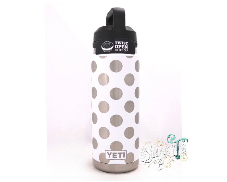 May include: A white Yeti water bottle with a silver polka dot pattern. The bottle has a black lid with the words "Twist Open to See Cap".