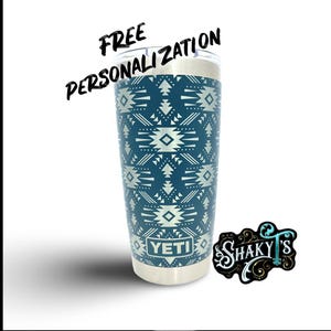 May include: A stainless steel Yeti tumbler featuring a blue and white geometric pattern. The tumbler has the word "YETI" printed on the bottom. The image also includes the text "FREE PERSONALIZATION" and a logo for "SHAKY'S".