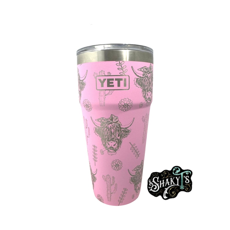 May include: Pink Yeti tumbler with a silver lid and a design of Highland cows and cacti. The tumbler has the word "YETI" printed on the side.