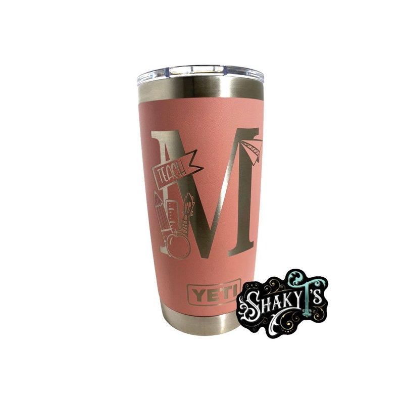May include: A pink YETI tumbler with a gold metallic design featuring the letter "M" and the word "Teach" with a pencil, ruler, and apple graphic.