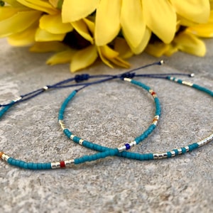 Op de afbeelding: Twee turquoise kralen armbanden met zilveren en gouden accenten. De armbanden zijn gebonden met een donkerblauw koord.