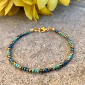 Pode incluir: Pulseira delicada de contas com contas turquesa, azul marinho e douradas. A pulseira &eacute; presa com um fecho dourado. Esta joia feita &agrave; m&atilde;o &eacute; perfeita para uso di&aacute;rio ou ocasi&otilde;es especiais.