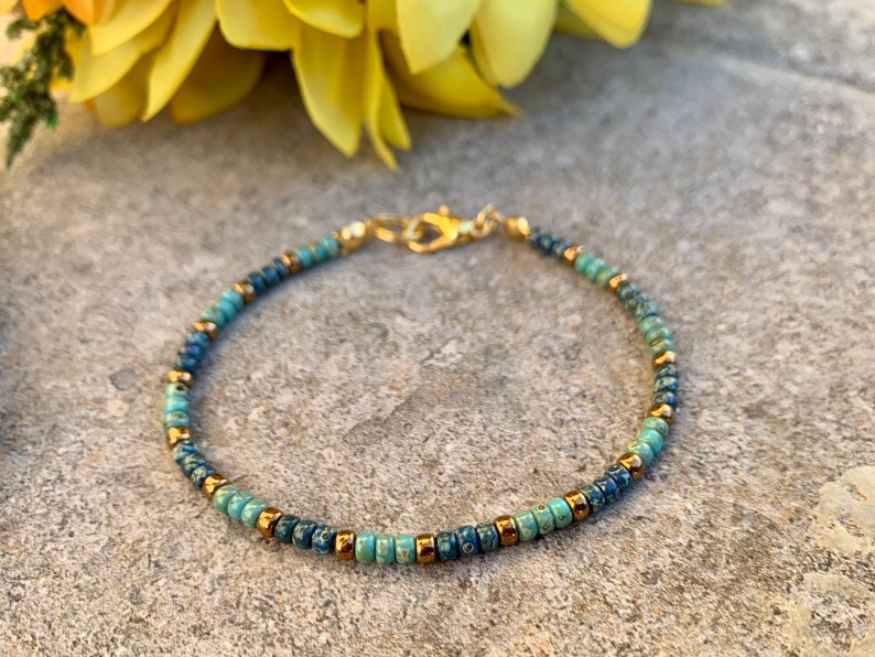 Pode incluir: Pulseira delicada de contas com contas turquesa, azul marinho e douradas. A pulseira &eacute; presa com um fecho dourado. Esta joia feita &agrave; m&atilde;o &eacute; perfeita para uso di&aacute;rio ou ocasi&otilde;es especiais.