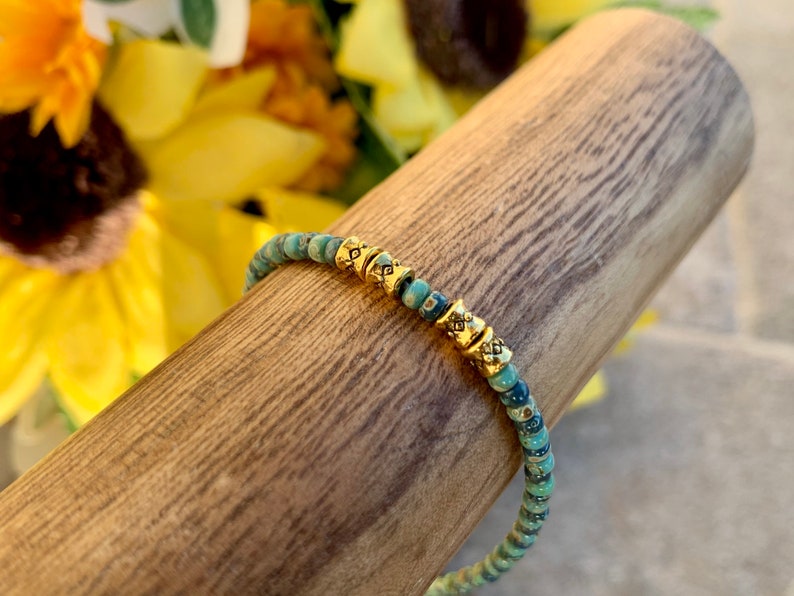 May include: A turquoise and gold beaded bracelet with a delicate design. The bracelet is made of small, round beads with a subtle shimmer. The gold beads are accented with a geometric pattern.