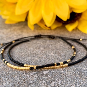 May include: Two delicate bracelets with black and gold beads. The bracelets are adjustable and have a simple, minimalist design.