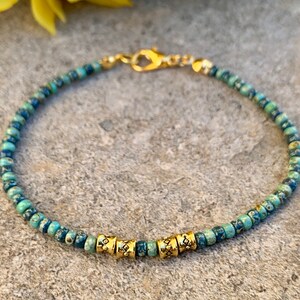 May include: A blue and green beaded bracelet with gold accents. The bracelet is made of small, round beads and has a clasp closure.