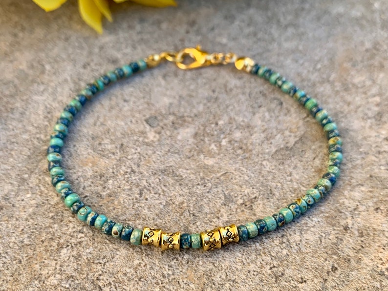 May include: A blue and green beaded bracelet with gold accents. The bracelet is made of small, round beads and has a clasp closure.