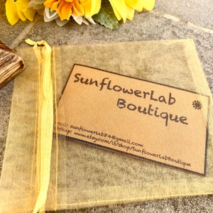 May include: A small, brown paper card with the text "SunflowerLab Boutique" and contact information for the shop. The card is sitting on top of a yellow mesh bag.