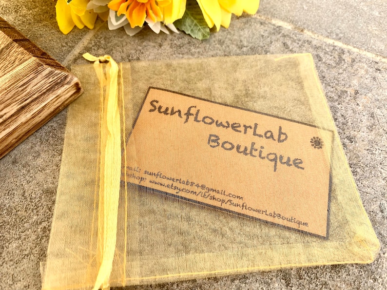 May include: A small, brown paper card with the text "SunflowerLab Boutique" and contact information for the shop. The card is sitting on top of a yellow mesh bag.