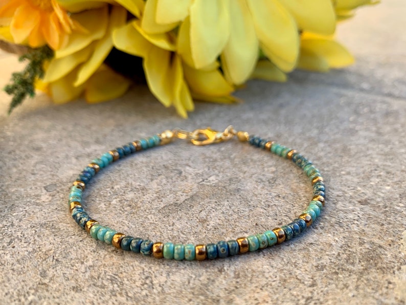 Pode incluir: Delicada pulseira de contas com uma mistura de contas azuis e turquesas e detalhes dourados. A pulseira &eacute; enfiada numa corrente dourada e tem um fecho. Uma joia elegante.