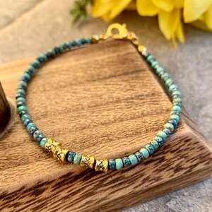 May include: A turquoise and blue beaded bracelet with gold accents. The bracelet has a clasp closure.
