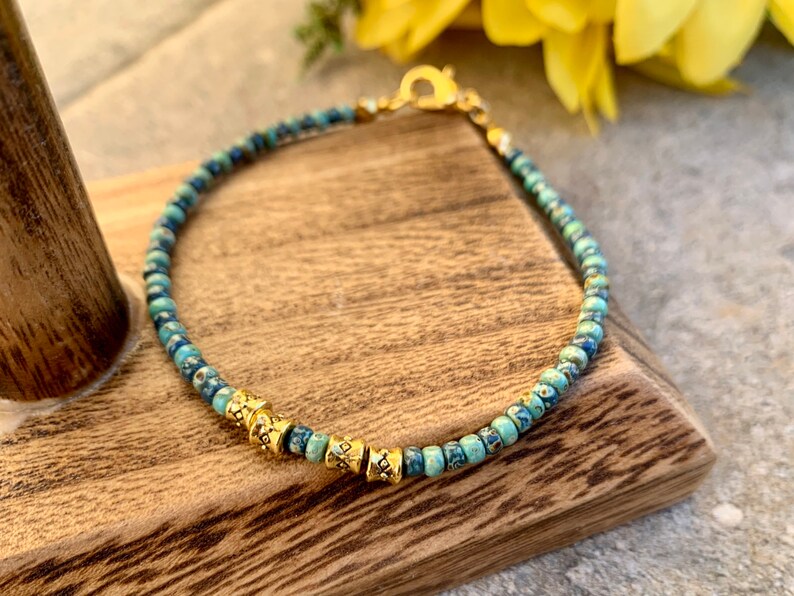 May include: A turquoise and blue beaded bracelet with gold accents. The bracelet has a clasp closure.