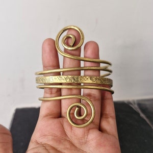 Könnte beinhalten: Ein goldfarbenes Metallarmband mit einer strukturierten Oberfläche und zwei Spiralmustern. Das Armband ist offen und verstellbar.