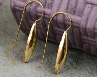 Puede incluir: Un par de pendientes colgantes de color dorado con un colgante largo, delgado y de forma ovalada. Los pendientes tienen un diseño simple y minimalista.
