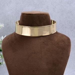 Puede incluir: Un collar choker de metal dorado en un maniquí de terciopelo marrón.