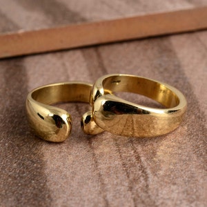 Op de afbeelding: Twee gouden ringen met een afgerond, glad ontwerp. De ringen zijn open en hebben een licht gebogen vorm.